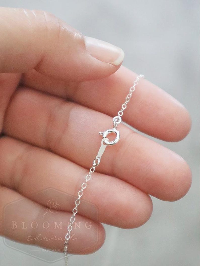 May include: A delicate silver chain necklace featuring a round spring ring clasp. The metal has a bright, reflective finish. A watermark with the text BLOOMING thread HANDMADE is visible in the lower left corner of the image.