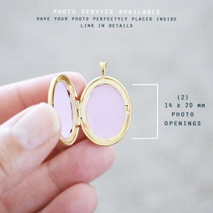 May include: A gold-colored oval locket, open to reveal two pink photo openings. The locket is held open, showcasing the interior. Text on the image reads: PHOTO SERVICE AVAILABLE, (2) 14 x 20 MM PHOTO OPENINGS.