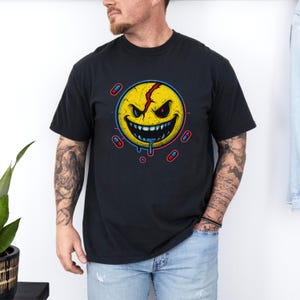 May include: Black t-shirt with a yellow, menacing smiley face design. The face has a red crack and dripping blue liquid, surrounded by red and blue pills. A distinctive graphic tee.