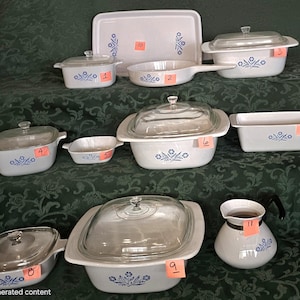 May include: A collection of white ceramic cookware with blue floral designs. The set includes various casserole dishes, a skillet, a serving tray, and a coffee pot. Each piece has a glass lid. The cookware is arranged on a green patterned surface.