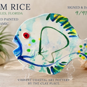 May include: Hand-painted ceramic fish plate with a vibrant coastal design. The plate features a light blue base with colorful accents of green, yellow, and blue. Signed and dated 9/91. Text on the plate reads "JIM RICE, NAPLES, FLORIDA, HAND PAINTED CERAMIC."