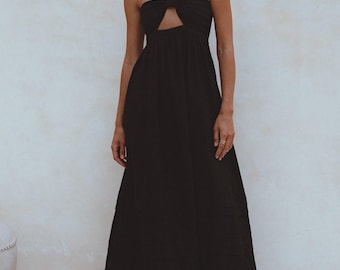 Può includere: Un abito lungo nero con collo all'americana e un ritaglio a forma di buco della serratura. L'abito presenta un corpetto aderente e una gonna fluida. La modella indossa sandali neri. Lo sfondo è di colore bianco sporco neutro.