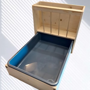 Peut inclure: Un mangeoire pour animaux de compagnie en bois avec un bac en plastique gris. Le mangeoire a un design rectangulaire avec une façade sectionnée et un plateau coulissant. Le bois est de couleur claire et le bac a un bord bleu.