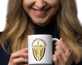 Peut inclure: Mug en céramique blanche avec l'inscription "SOURCE UNITED" et un emblème doré et marron d'une épée et d'un bouclier. La tasse a une anse standard et une finition brillante. Le design est centré sur la tasse.