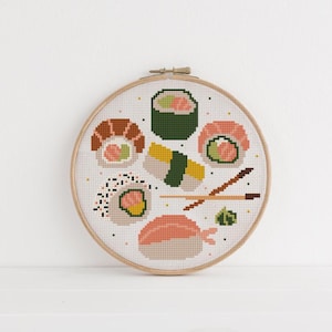 Könnte beinhalten: Ein Kreuzstich-Stickrahmen mit verschiedenen Sushi-Rollen und Nigiri. Das Design umfasst Lachs-, Garnelen- und Avocado-Sushi sowie Essstäbchen und Wasabi. Die Stickerei befindet sich vor einem weißen Hintergrund in einem Holzrahmen.