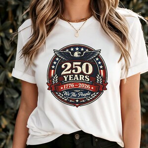 Peut inclure: T-shirt blanc avec un motif circulaire comm&eacute;morant 250 ans, de 1776 &agrave; 2026. Le motif pr&eacute;sente un aigle, des &eacute;toiles et le texte "250 YEARS" et "We The People" dans un code couleur patriotique rouge, blanc et bleu.