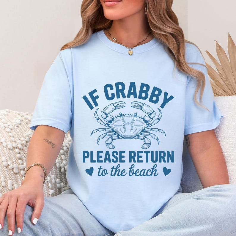 Puede incluir: Camiseta azul claro con el texto "IF CRABBY PLEASE RETURN to the beach" y un gr&aacute;fico de cangrejo. El cangrejo y el texto son de color azul oscuro. La camiseta es de manga corta.