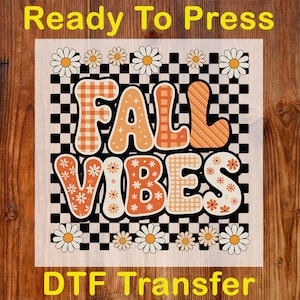 May include: A DTF transfer with the words "FALL VIBES" in orange, white, and brown, with daisy and checkerboard patterns. The words "Ready To Press" and "DTF Transfer" are also printed on the transfer.