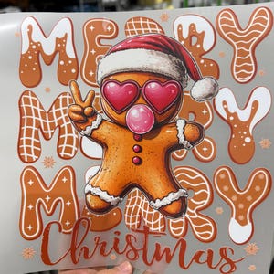 Op de afbeelding: Een feestelijk kerstontwerp met een peperkoekmannetje met een kerstmuts en hartvormige zonnebril, die een bel blaast. De woorden "MERRY CHRISTMAS" worden weergegeven in peperkoek-lettertype, met sneeuwvlokaccenten.