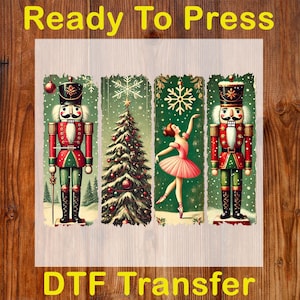 May include: A DTF transfer featuring a Christmas theme. The design includes two nutcrackers in red, green, and black, a decorated Christmas tree, and a ballerina in a pink tutu. The words "Ready To Press" and "DTF Transfer" are in yellow.