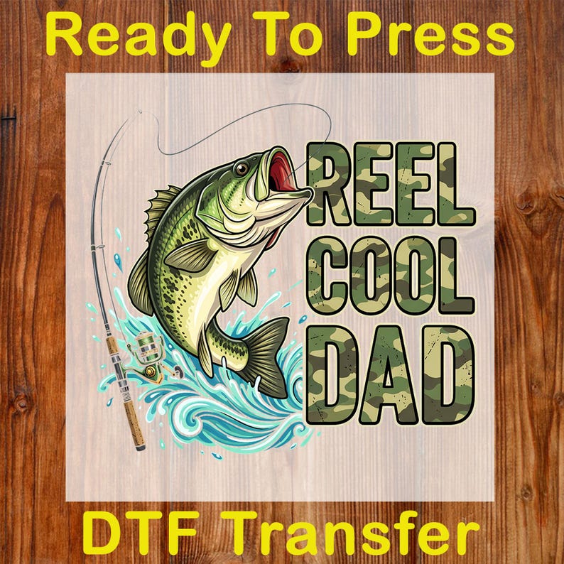 Pu&ograve; includere: Trasferimento DTF con un pesce persico verde e giallo che salta dall'acqua blu, con una canna da pesca. Il testo "REEL COOL DAD" &egrave; in lettere mimetiche, con "Ready To Press" e "DTF Transfer" in giallo.