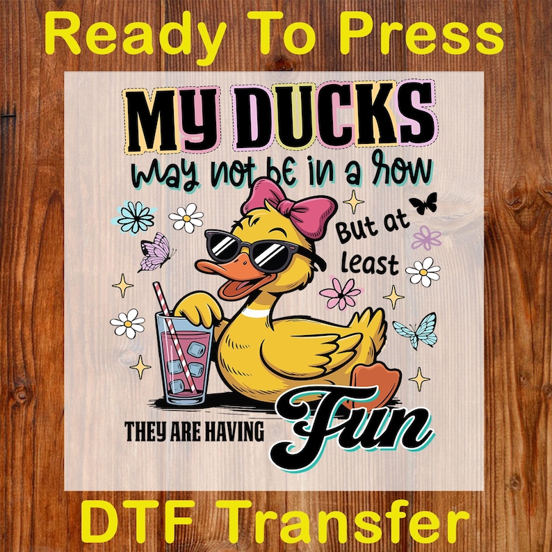 May include: A DTF transfer featuring a cartoon duck wearing sunglasses and a pink bow, holding a drink with ice. The text reads "MY DUCKS may not be in a row But at least THEY ARE HAVING Fun."