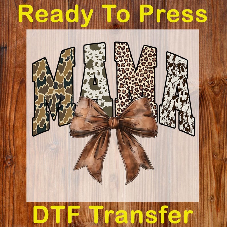 May include: A DTF transfer featuring the word "MAMA" in a mix of camouflage, cow print, and leopard print patterns. A large brown bow is centered below the word. The text "Ready To Press" and "DTF Transfer" are displayed in yellow.