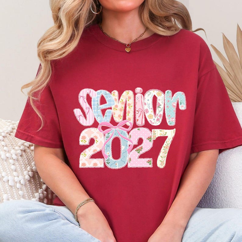 Peut inclure: Un t-shirt bordeaux avec le mot "Senior" et l'ann&eacute;e "2027" dans un design floral color&eacute;. Le texte est dans une police ludique, avec un accent de n&oelig;ud. Le t-shirt est de style confortable et d&eacute;contract&eacute;.