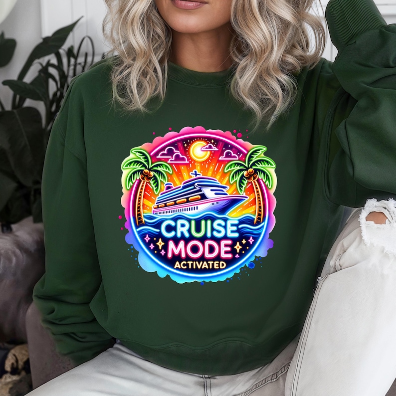 May include: Dark green sweatshirt featuring a vibrant graphic. The graphic includes a cruise ship, palm trees, and the words "CRUISE MODE ACTIVATED" in a neon-style design. The design is set against a backdrop of a sunset and ocean waves.