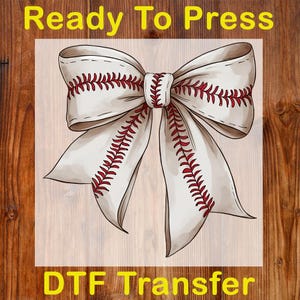 May include: A DTF transfer featuring a baseball-themed bow design. The bow is white with red stitching, resembling a baseball. The words "Ready To Press" and "DTF Transfer" are in yellow.