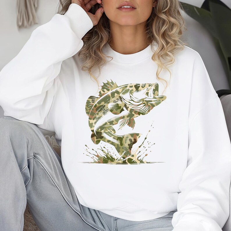 Puede incluir: Sudadera blanca con un gran gr&aacute;fico de un pez saltando en un patr&oacute;n de camuflaje. El pez se representa con escamas y aletas detalladas, con salpicaduras de agua a su alrededor. La sudadera tiene mangas largas y cuello redondo.