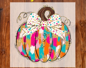 May include: A colorful DTF transfer featuring a pumpkin design. The pumpkin has a brown stem and a large bow with polka dots. The pumpkin is painted with pink, orange, and teal brushstrokes, with gold glitter accents. The words "Ready To Press" and "DTF Transfer" are in yellow and black.