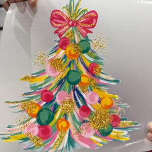 Op de afbeelding: Een kleurrijk kerstboomontwerp met een rode strik. De boom heeft penseelstreken van roze, geel, groen en blauw, versierd met ronde ballen in verschillende kleuren en gouden glitteraccenten. Een feestelijk vakantiethema.