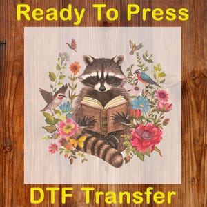 May include: A DTF transfer featuring a raccoon reading a book, surrounded by colorful flowers and birds. The text "Ready To Press" and "DTF Transfer" are in yellow.