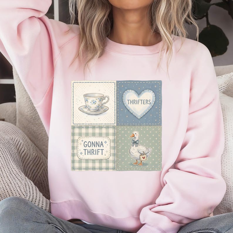 May include: A light pink sweatshirt with a patchwork design featuring a teacup, a heart with the word "Thrifters", a goose, and the text "Gonna Thrift". The design is in shades of blue, green, and white.