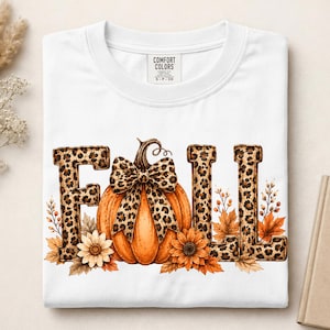 May include: A white t-shirt featuring the word FALL in a leopard print pattern. The letter A is replaced by an orange pumpkin adorned with a leopard print bow. The design includes orange and brown autumn leaves and sunflowers at the base.