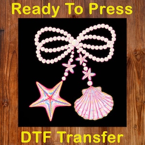 May include: A DTF transfer design featuring a pearl bow, starfish, and seashell on a black background. The starfish and seashell have pink, blue, and yellow accents. The words "Ready To Press" and "DTF Transfer" are in yellow.