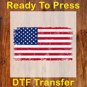 May include: A distressed American flag design in red, white, and blue, with the text "Ready To Press" at the top and "DTF Transfer" at the bottom. The flag features stars and stripes, ideal for patriotic projects.