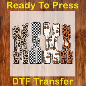 May include: A DTF transfer with the word "MAMA" in a bold, decorative font. The letters feature various patterns: leopard print, black and white checkerboard, and a pumpkin design. The words "Ready To Press" and "DTF Transfer" are also visible.