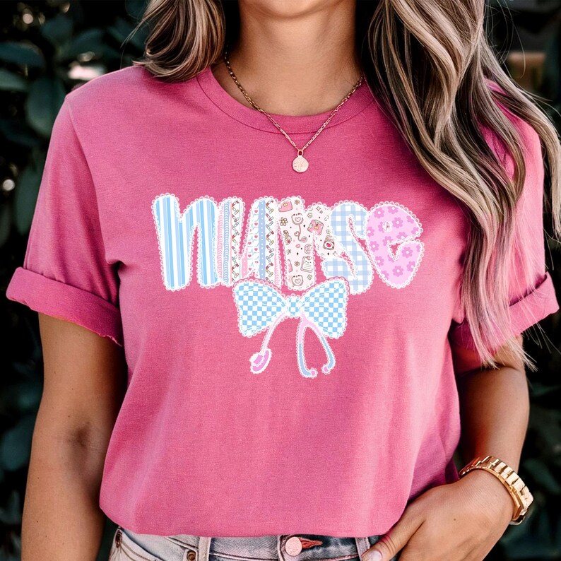 May include: A pink t-shirt with the word "NURSE" in a patchwork design. The letters are in various patterns, including blue stripes, gingham, and floral prints. A blue and white bow and a stethoscope graphic are below the word.
