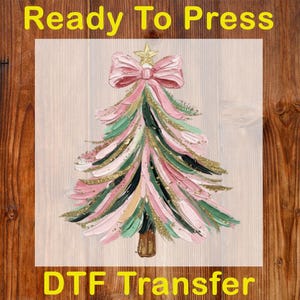 May include: A colorful Christmas tree design with pink, green, and gold brushstrokes. The tree is topped with a pink bow and a gold star. The words "Ready To Press" and "DTF Transfer" are printed in yellow.