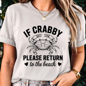 Puede incluir: Camiseta gris claro con el texto "IF CRABBY PLEASE RETURN to the beach" y una ilustraci&oacute;n de un cangrejo. El cangrejo es blanco y negro. La camiseta tiene mangas cortas y cuello redondo.