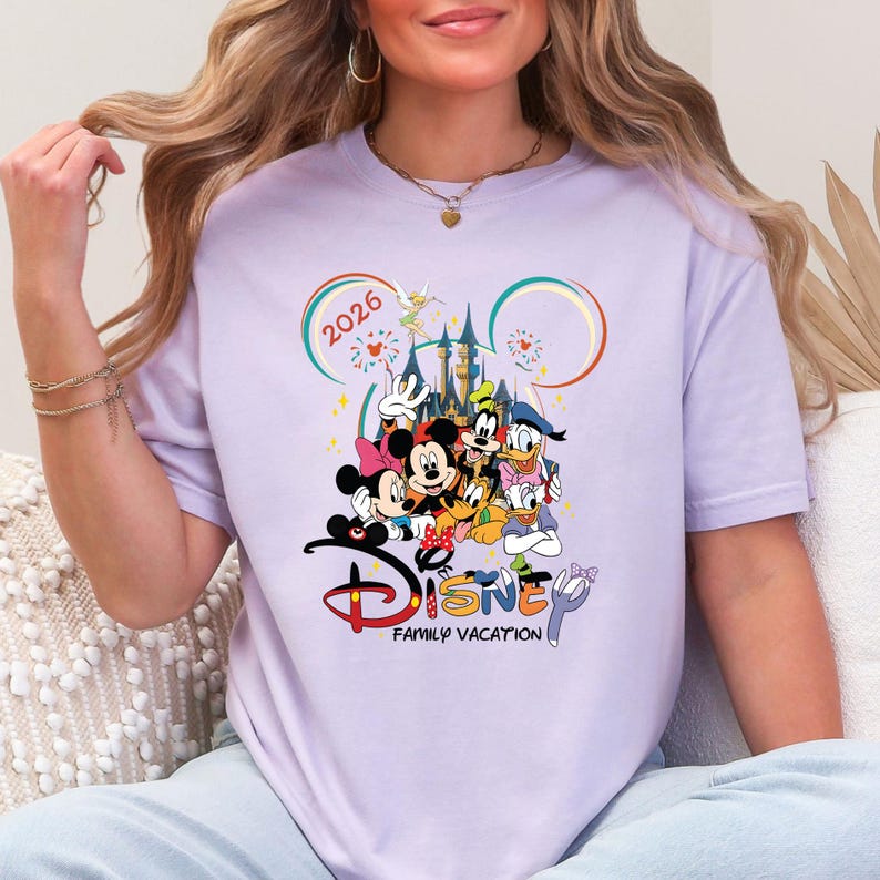 May include: A lilac t-shirt with a Disney graphic. The design features Mickey and Minnie Mouse, Goofy, Donald Duck, and other characters, with the text "Disney Family Vacation" and the year "2026".