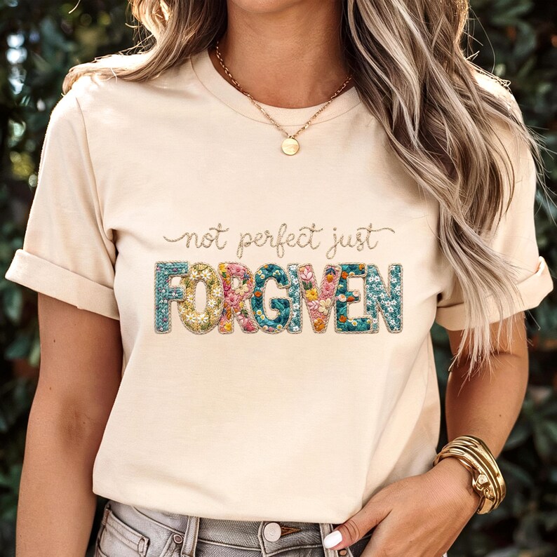 Op de afbeelding: Beige t-shirt met de tekst "not perfect just FORGIVEN". Het woord "FORGIVEN" is in een kleurrijk bloemenpatroon, terwijl de andere tekst in een cursief lettertype staat.