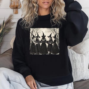 Puede incluir: Sudadera negra con un gr&aacute;fico de cinco brujas con vestidos y sombreros negros, sobre un fondo de bosque. El texto "Girls Will Be Girls" est&aacute; impreso en el gr&aacute;fico. Cuello redondo.