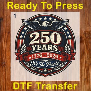 Peut inclure: Un transfert DTF avec un motif patriotique. Le motif pr&eacute;sente un embl&egrave;me circulaire avec un aigle, des &eacute;toiles et le texte "250 YEARS 1776-2026 We The People". Les mots "Ready To Press" et "DTF Transfer" sont &eacute;galement pr&eacute;sents.