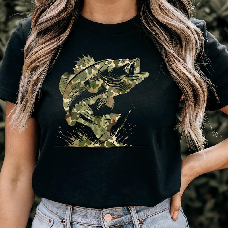 Puede incluir: Camiseta negra con un dise&ntilde;o de un pez lubina saltando. El pez tiene un patr&oacute;n de camuflaje en verde, marr&oacute;n y beige. Salpicaduras de agua alrededor del pez. Un dise&ntilde;o para los entusiastas de la pesca.