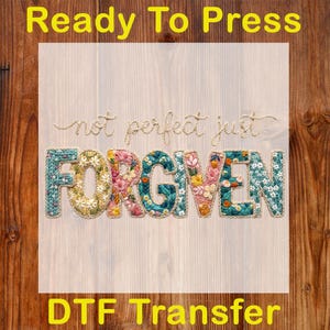Op de afbeelding: Een DTF-transfer met de tekst "not perfect just FORGIVEN" in een bloemenontwerp. Het woord "FORGIVEN" staat in grote, kleurrijke letters. De tekst "Ready To Press" en "DTF Transfer" zijn geel.