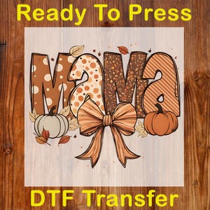 May include: A DTF transfer with the word "MAMA" in brown, orange, and cream colors, decorated with fall leaves, pumpkins, and a large bow. The text "Ready To Press" and "DTF Transfer" are in yellow.