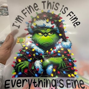 Peut inclure: Graphique du Grinch, portant un bonnet de P&egrave;re No&euml;l et des guirlandes lumineuses, avec le texte "I'm Fine. This is Fine. Everything's Fine." Le Grinch est vert et affiche une expression renfrogn&eacute;e.
