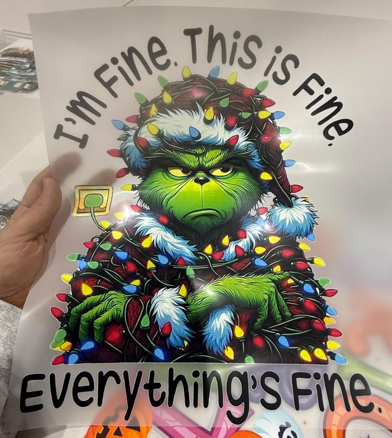 Może przedstawiać: Grafika przedstawiająca postać Grincha w czapce Świętego Mikołaja i owiniętego w lampki choinkowe. Tekst brzmi: "I'm Fine. This is Fine. Everything's Fine."