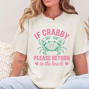 Puede incluir: Camiseta color crema con el texto "IF CRABBY PLEASE RETURN to the beach" en rosa, con un gr&aacute;fico de cangrejo verde. La camiseta tiene un dise&ntilde;o informal con tem&aacute;tica de playa.