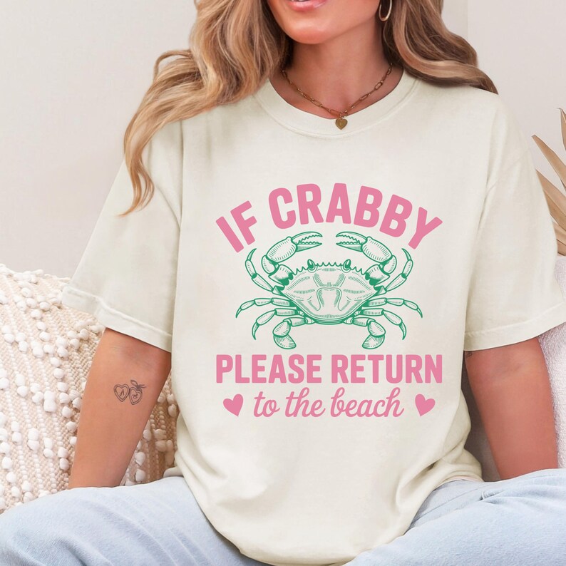 Puede incluir: Camiseta color crema con el texto "IF CRABBY PLEASE RETURN to the beach" en rosa, con un gr&aacute;fico de cangrejo verde. La camiseta tiene un dise&ntilde;o informal con tem&aacute;tica de playa.