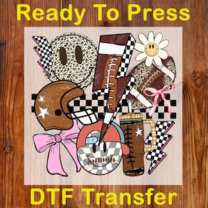 Peut inclure: Transfert DTF avec un collage de graphiques sur le th&egrave;me du sport. Comprend un ballon de football am&eacute;ricain, un casque, des visages souriants, des &eacute;clairs et une marguerite. Les mots "Ready To Press" et "DTF Transfer" sont imprim&eacute;s.