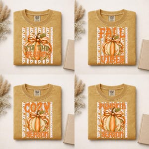 May include: Four mustard yellow crewneck t-shirts featuring autumn-themed graphics. Each shirt displays a pumpkin illustration with vertical stripes and text including 'Tis the Season', 'Fall Vibes', 'Cozy', and 'Pumpkin' in orange and white.
