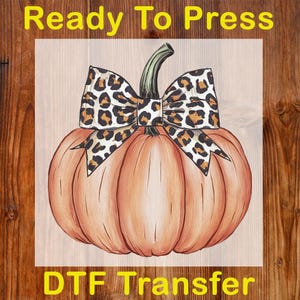 May include: A watercolor-style pumpkin with a leopard print bow. The pumpkin is orange with a green stem. The words "Ready To Press" and "DTF Transfer" are in yellow text.