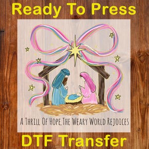 May include: A DTF transfer featuring a nativity scene with a colorful bow and star accents. The image includes the text "Ready To Press" and "A THRILL OF HOPE, THE WEARY WORLD REJOICES". The design is set against a wood grain background.