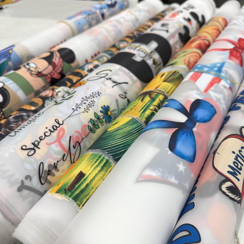 May include: A collection of rolled fabric featuring various designs. Some rolls display cartoon characters, floral patterns, and patriotic themes with red, white, and blue colors. Other rolls have text that reads "Special, lovely, unique" and "God".