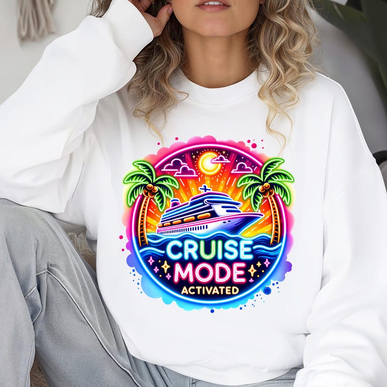 May include: White sweatshirt featuring a colorful graphic of a cruise ship on the ocean with palm trees and the words "CRUISE MODE ACTIVATED". The design is in a vibrant, neon style, perfect for vacation.