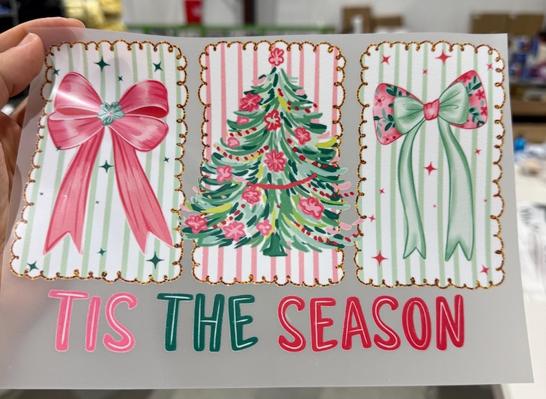 Op de afbeelding: Een kerstontwerp met drie rechthoekige frames met een gouden glitterrand. De frames tonen een roze strik, een kerstboom en een groene strik. De tekst "TIS THE SEASON" is geschreven in roze en groen.